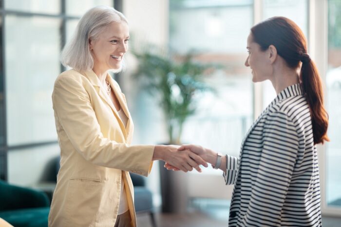 Photo of senior employee and millennial employee shaking hands illustrates blog "3 Ideas to Combat Ageism in the Workplace"