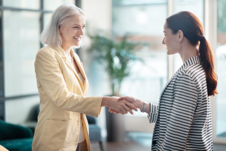 Photo of senior employee and millennial employee shaking hands illustrates blog "3 Ideas to Combat Ageism in the Workplace"