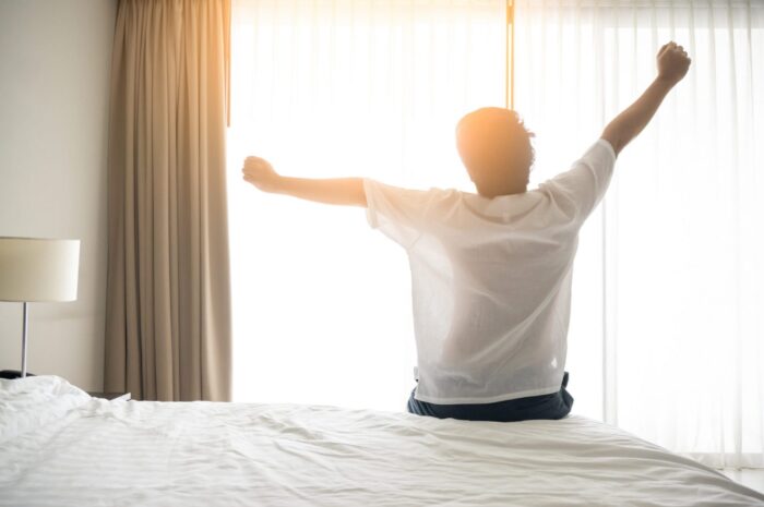 Photo of man stretching arms in bed illustrates blog: "Easy Hacks to Improve the Quality of Your Sleep"