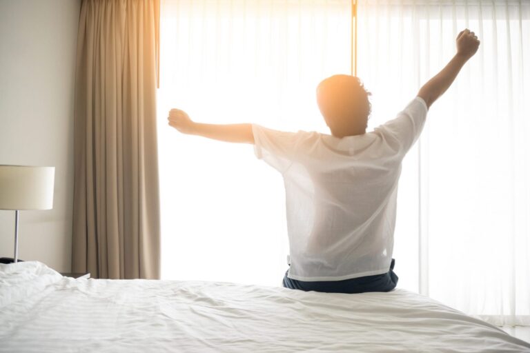 Photo of man stretching arms in bed illustrates blog: "Easy Hacks to Improve the Quality of Your Sleep"