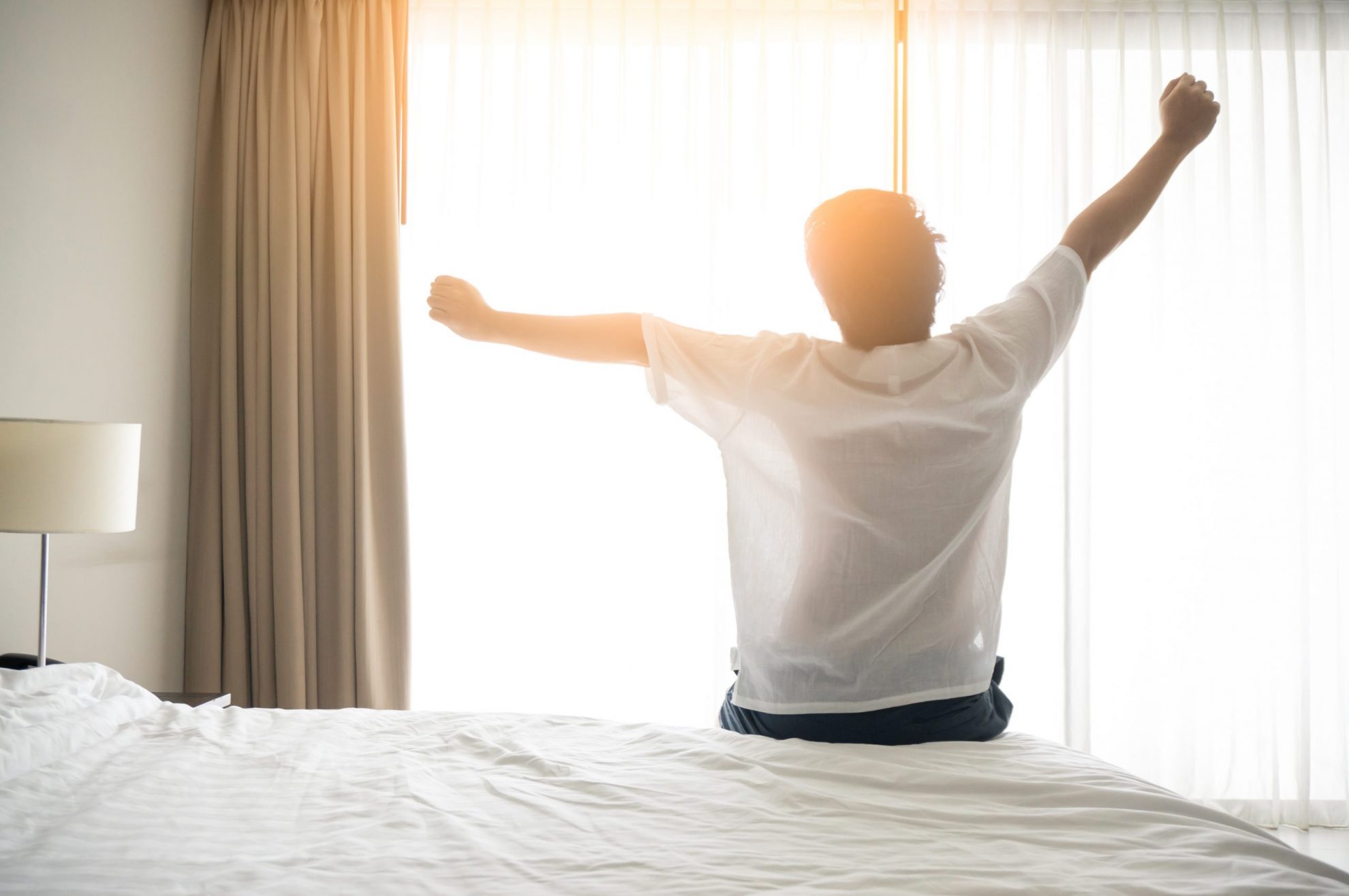 Photo of man stretching arms in bed illustrates blog: "Easy Hacks to Improve the Quality of Your Sleep"