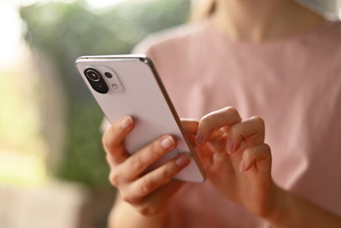 Photo of woman holding smartphone illustrates blog: "This Holiday Season, Beware of Package Delivery Scams"