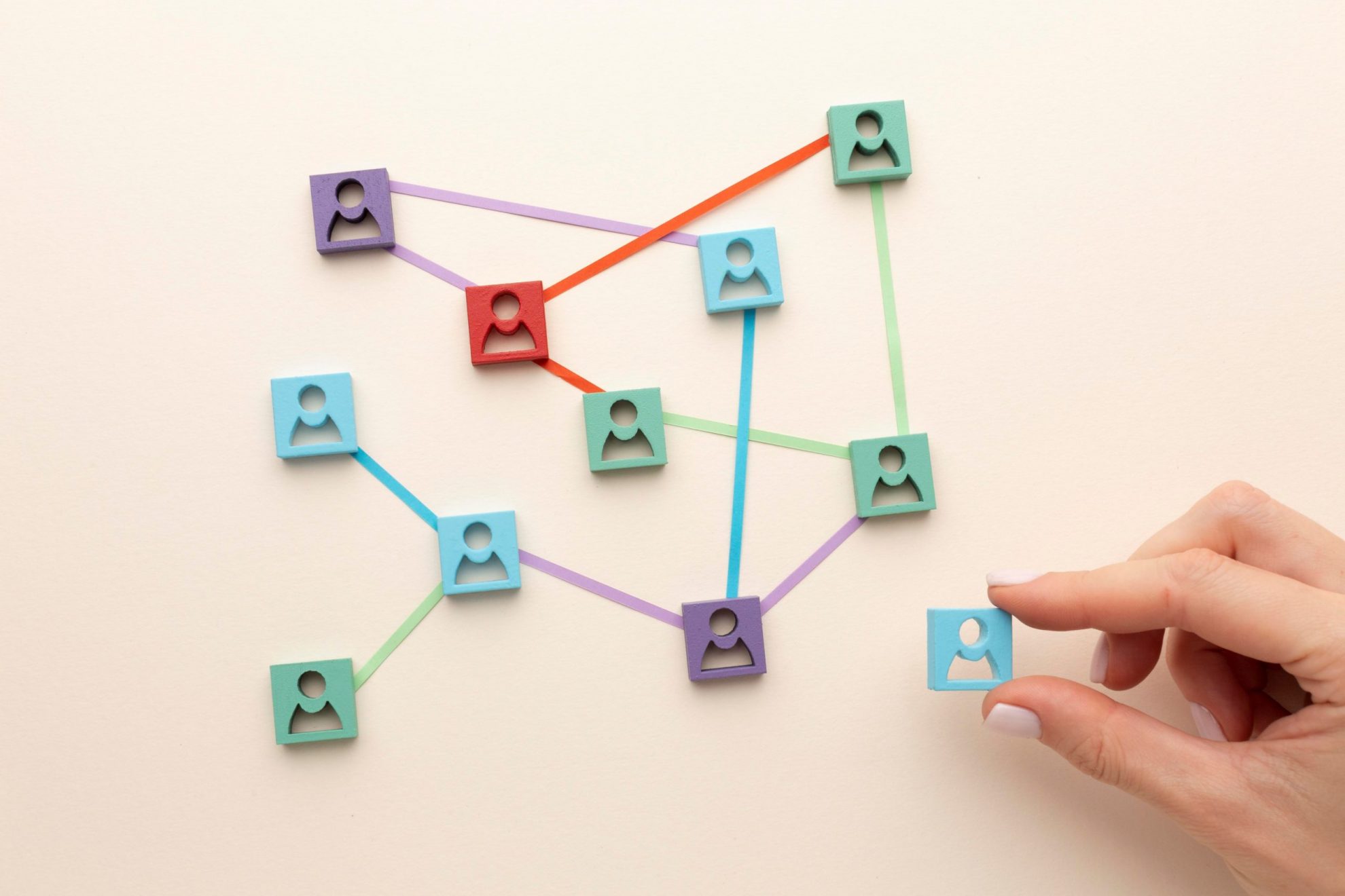 Close-up of hand arranging pieces with icons of people united by strings illustrates blog "Get Your Networking Skills to the Next Level"