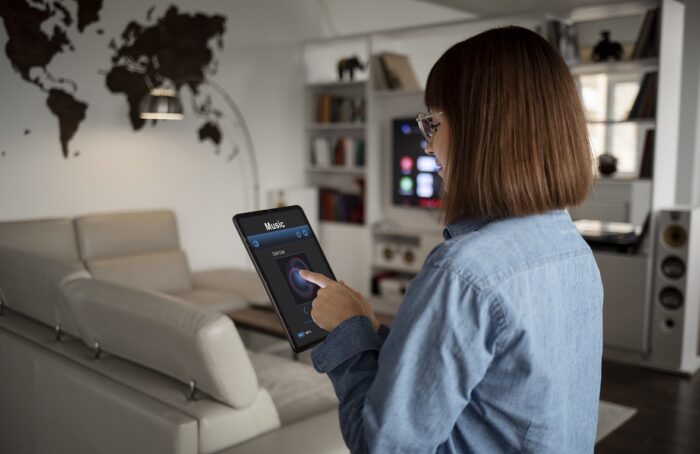internet-of-things-fp Woman standing in living room holding tablet that reads "Music" illustrates blog "What Is the Internet of Things (IoT)?"