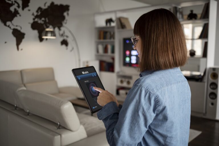 Woman standing in living room holding tablet that reads "Music" illustrates blog "What Is the Internet of Things (IoT)?"