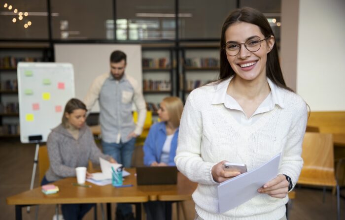 Businesswoman smiling with people working in the backgrouund illustrates blog "Hiring Tips to Help You Find the Right Employees"