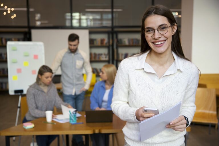 Businesswoman smiling with people working in the backgrouund illustrates blog "Hiring Tips to Help You Find the Right Employees"