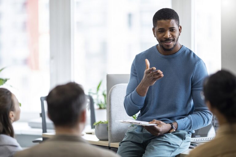 Man sitting on desk talking to people illustrates blog "The Importance of Fostering a Culture of Learning in Your Organization"