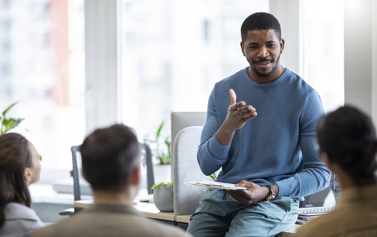 learning-fp Man sitting on desk talking to people illustrates blog "The Importance of Fostering a Culture of Learning in Your Organization"